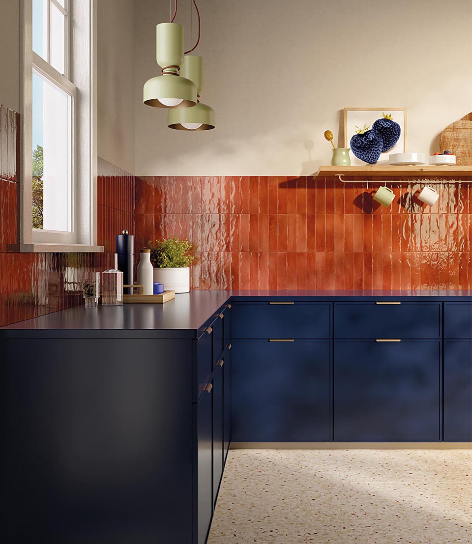 A modern kitchen featuring deep blue cabinetry and a dark countertop offset by glossy, reddish-orange splashback tiles arranged vertically.